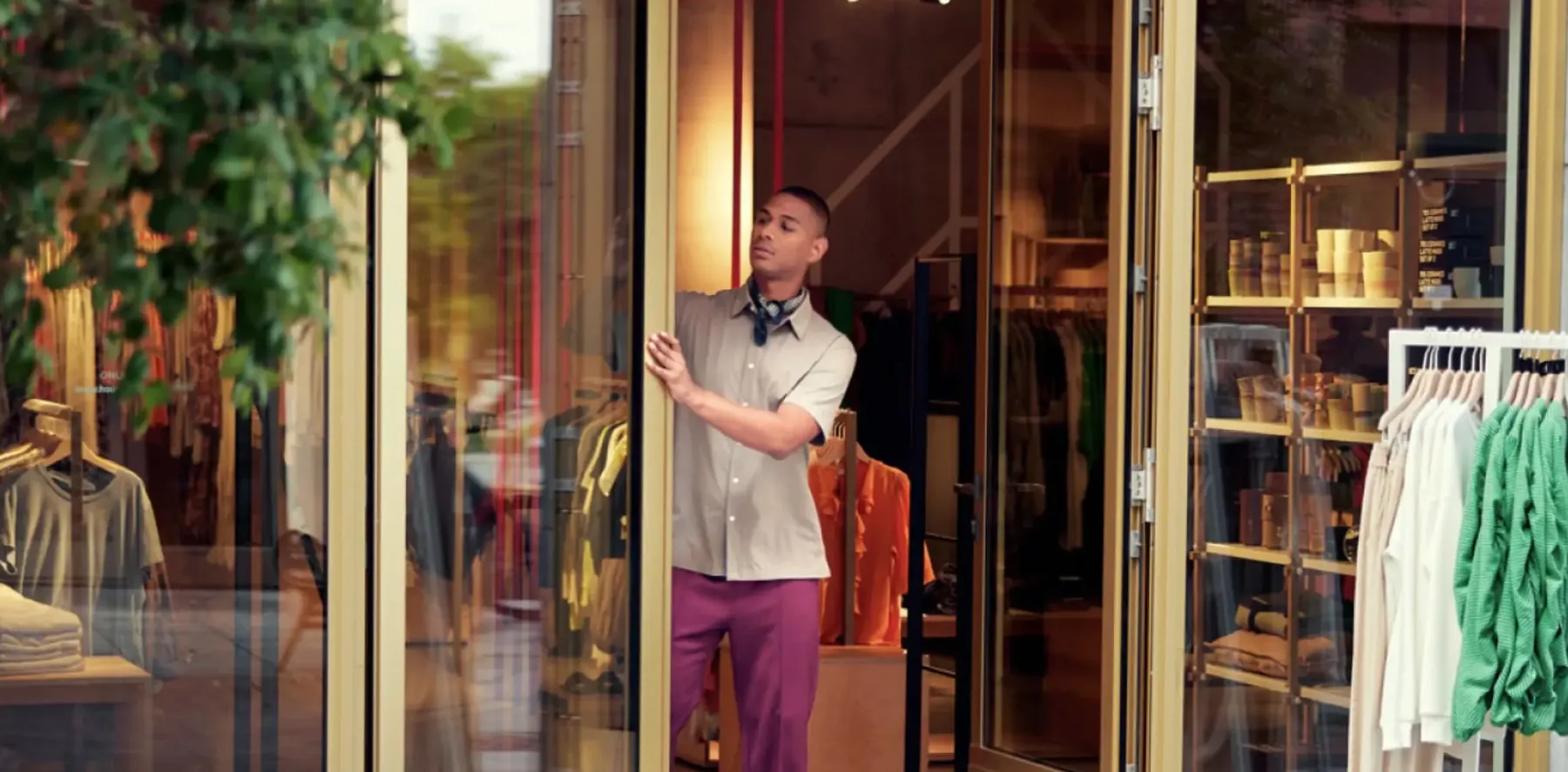 Person dressed in a grey button-down shirt and purple pants in the doorway of a clothing store.