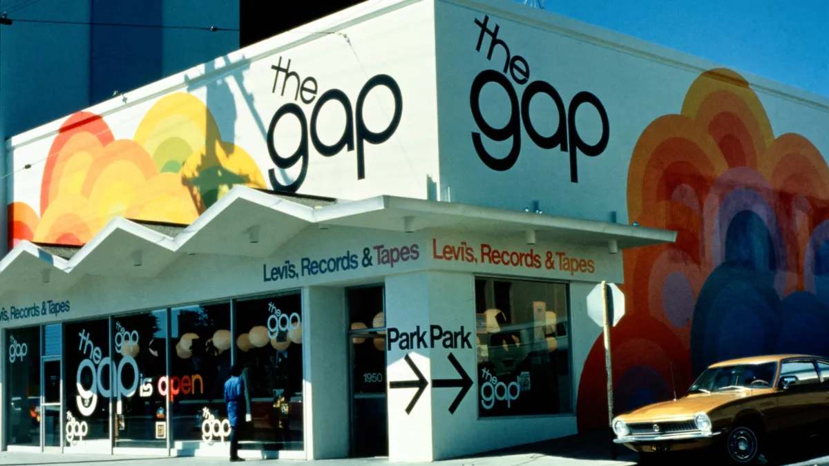 A person window shops at store at a street corner. An orange corner is parked on the right, next to a stop sign.