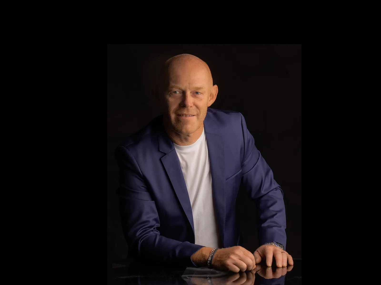 A person in a blue suit and a white T-shirt poses against a black background.