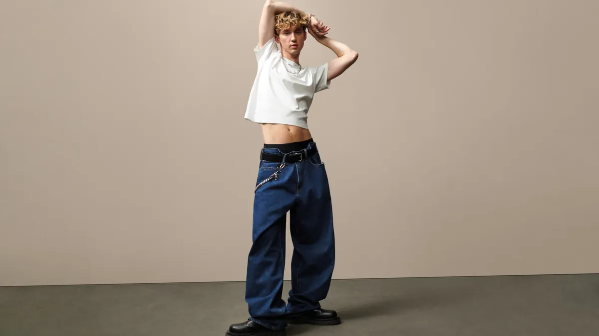 Singer Troye Sivan, wearing a white tee and loose-cut jeans, stands in front of beige background in an ad for Gap