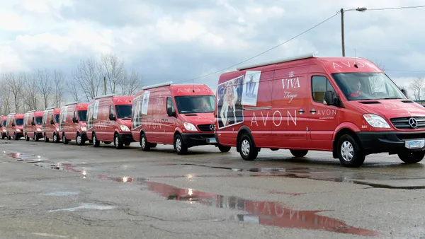 A row of pink vans line up on a single road, with "Avon" printed on the side of each.