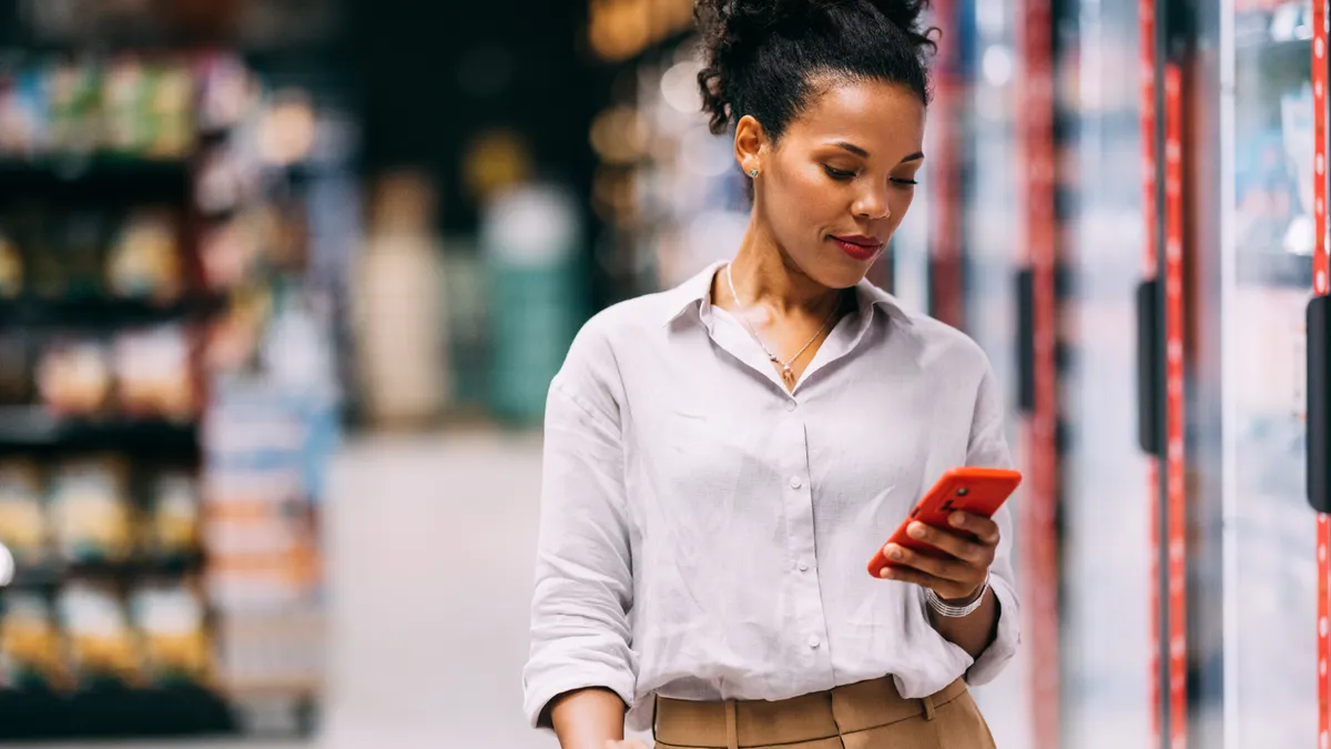 Woman looking at her mobile phone while shopping at the supermarket.