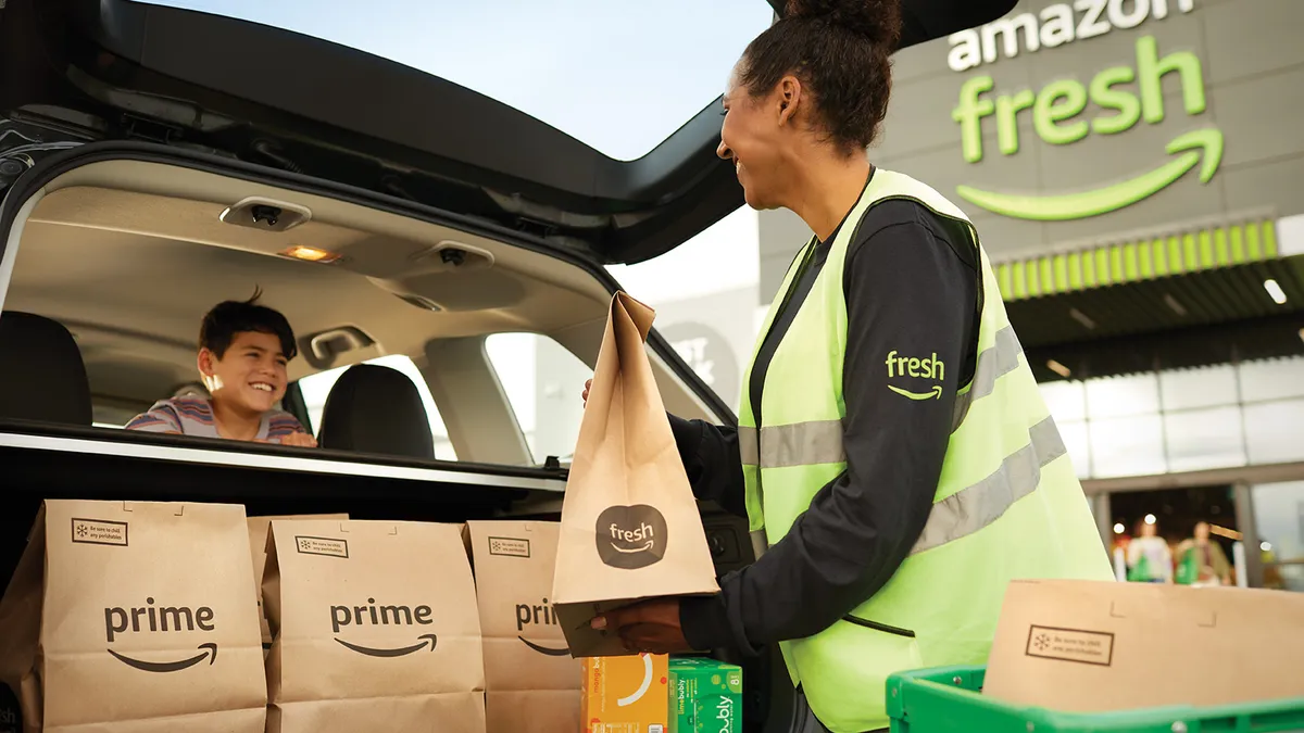 Amazon employee loading brown paper grocery bags into car trunk