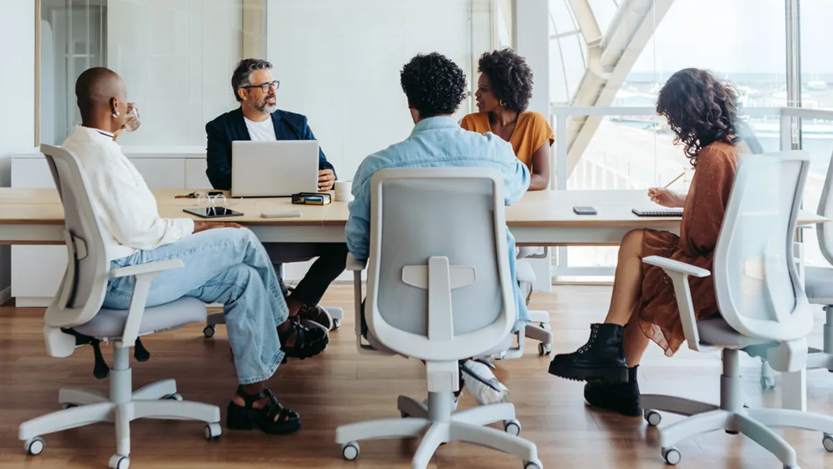 6 people dressed in business casual clothing sitting around a conference table having a meeting